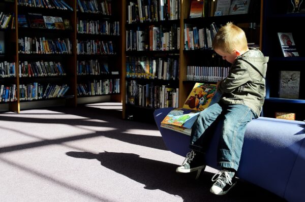 Poika lukee kirjaa kirjahyllyjen edessä.